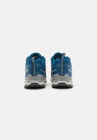 Des chaussures de sport bleues avec une tige en maille texturée, des accents gris et une semelle en caoutchouc. Elles présentent des languettes de traction en boucle et un branding minimal.