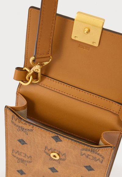 Τσάντα χειρός από ταμπά δέρμα με χρυσά μεταλλικά στοιχεία, που διαθέτει ένα μοτίβο με το λογότυπο και δομημένο σχήμα. Το εσωτερικό έχει λεία επιφάνεια και έναν ενιαίο θάλαμο.