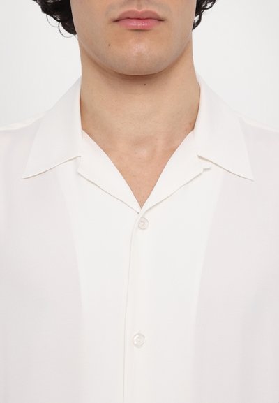 Camicia bianca a maniche corte con bottoni, in tessuto liscio, colletto classico e bottoni simili a perle; design minimalista, tessuto leggero.