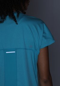 Teal sportströja med korta ärmar, med en rektangulär design på baksidan, en reflekterande rand och "D1" tryckt i en kontrasterande färg.