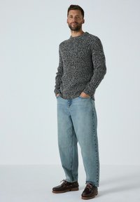 Pulover gri tricotat cu guler rotund, asociat cu blugi largi de culoare albastru deschis și pantofi maro închis cu șireturi albe și talpă texturată.