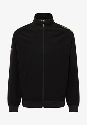 Sort zip-jakke med høj krave, ribbede manchetter og kant. Har logo-detaljer på skulderen og en glat stofstruktur.