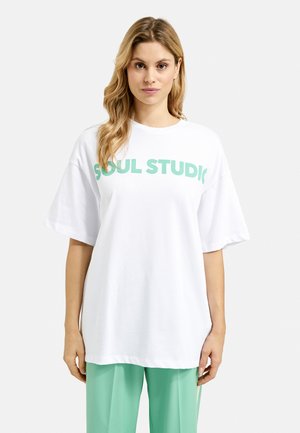 Weißes, übergroßes T-Shirt mit großen grünen Texten, die "SOUL STUDIO" lesen. Das Shirt hat kurze Ärmel und einen runden Ausschnitt.