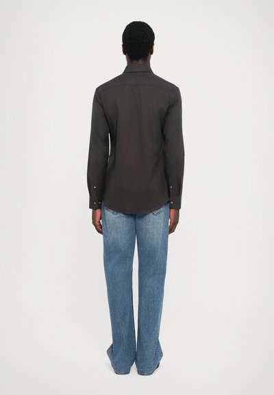 Svart skjorte med lange ermer, med buet kant og skreddersydd bak, sammen med løstsittende, lyseblå jeans.