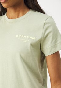 Lys grønn bomulls t-skjorte med rund hals, korte ermer, og preget hvit tekst som sier "BJÖRN BORG STOCKHOLM 1956" på brystet.