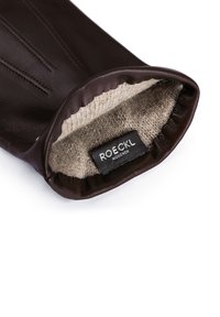 Braune Lederhandschuhe mit einem weichen, beige gefütterten Innenleben. Verfügt über genähte Details an der Außenseite und ein Etikett mit der Aufschrift "ROECKL MÜNCHEN."