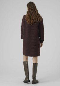 Vestito a maglia bordeaux con un motivo a zig zag testurizzato, maniche lunghe e un orlo sopra il ginocchio, abbinato a stivali di pelle marroni alti fino al ginocchio.