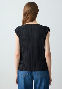 Top plissettato nero con maniche corte, caratterizzato da una texture liscia e una linea dritta, abbinato a jeans in denim blu a vita alta.