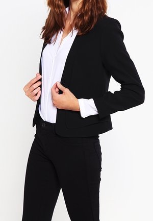 Svart figursydd kavaj med en slät yta, strukturerade slag och långa ärmar, i kombination med en vit skjorta med knappar och svarta byxor.