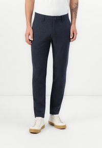 Pantalones azul marino de tejido texturizado con corte ajustado, que cuentan con un cierre de botón y bolsillos laterales, combinados con zapatillas blancas.
