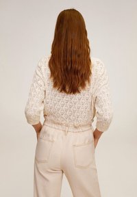 Kremowy sweter robiony na drutach z diamentowym wzorem i rękawami o długości trzech ćwierć, zestawiony z beżowymi spodniami o wysokim stanie z elastycznym paskiem.