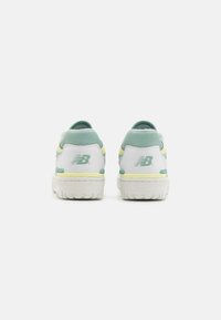Zapatillas blancas con acentos verde claro y detalles amarillos. Parte superior texturizada con cuello acolchado y diseño del logo en el talón. Suela de goma.