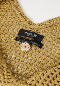 Top en tricot jaune moutarde, avec un design en crochet lâche. Comprend un bouton doré proéminent et une étiquette noire avec "REPLAY" et "Tricot fait main."