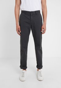 Šedé bavlněné kalhoty s přímým střihem, zapínáním na knoflíky, bočními kapsami a ohrnutými manžetami. Kombinovány s bílými teniskami.