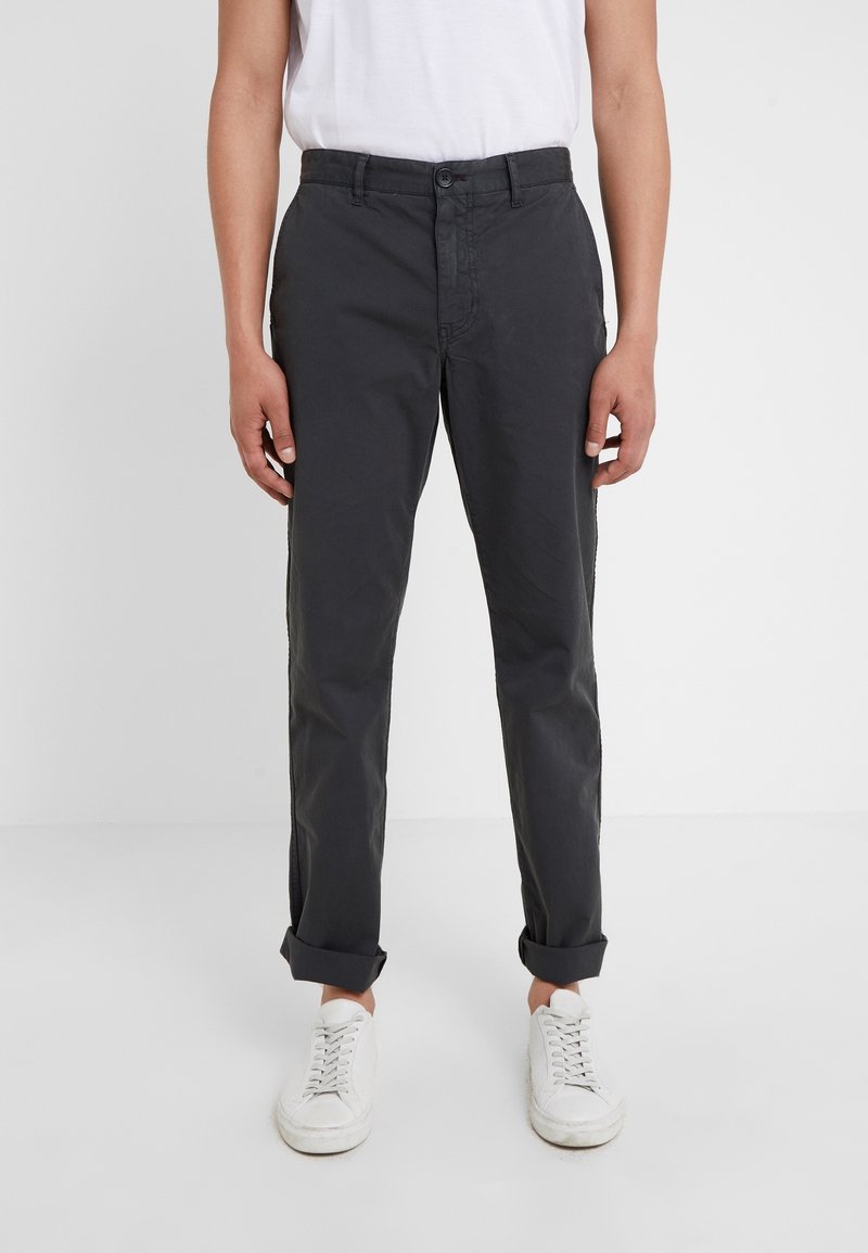 Šedé bavlněné kalhoty s přímým střihem, zapínáním na knoflíky, bočními kapsami a ohrnutými manžetami. Kombinovány s bílými teniskami.