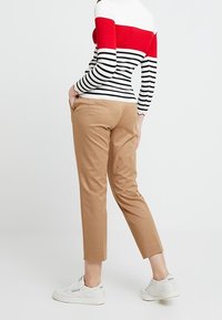 Pull rayé aux couleurs rouge, blanc et noir ; pantalon beige ; baskets blanches. Le pantalon présente une coupe droite avec des chevilles retroussées.