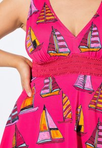 Fuksia mekko, jossa on syvä V-pääntie, värikkäitä purjeveneprinttejä eri kuvioissa, ja jonka vyötäröllä on smokkimekko, joka tuo asulle muotoa.