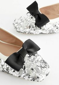Ballet-latkat päällystetty hopea- ja mustilla paljeteilla, joissa on musta nauhabow etuosassa ja beige sisävuori.