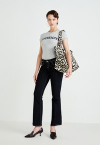 Woman wearing a gray "Copenhagen" t-shirt, dark jeans, black heels, hoop earrings, and carrying a large leopard print tote bag on her shoulder.