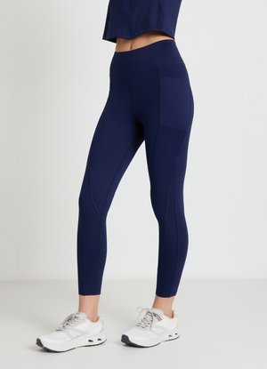 Navy leggings made from stretch fabric feature a high waistband, flat seams, and side pockets. Paired with white athletic shoes.