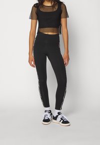 Black mesh cropped top with short sleeves, paired with high-waisted black leggings featuring white side stripes and black sneakers.