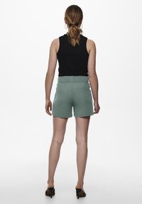 Pantaloni corti verdi con elastico in vita, dalla vestibilità rilassata e superficie liscia, abbinati a un top senza maniche nero, visti da dietro.