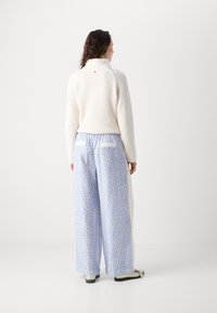 Pull crème à côtes avec un col montant, associé à un pantalon large à motifs bleu clair, doté d'un cordon de serrage et de poches.