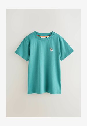 Teal bomulds t-shirt med korte ærmer, ribbet rund halsudskæring og et lille broderet design på brystet. Glat tekstur, afslappet stil.
