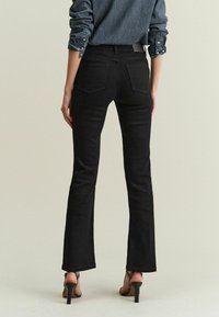 Zwarte flared jeans met een gladde textuur, voorzien van twee achterzakken en een middelhoge taille, gecombineerd met zwarte haksandalen.
