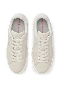 Ανοιχτό μπεζ σουέντ αθλητικά παπούτσια με στρογγυλερή μύτη, επίπεδα κορδόνια και λευκή λαστιχένια σόλα. Εσωτερικά διαθέτουν κόκκινη σήμανση σε γκρι πάτο.