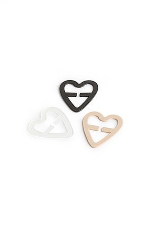 Tres clips en forma de corazón de plástico en negro, blanco y beige, con diseños recortados y superficies lisas.