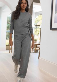 Gråt, blødt stofoutfit bestående af en wraps-style langærmet top og brede bukser, parret med lette sneakers.