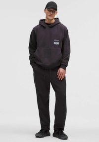 Mørk lilla hoodie med frontlomme, trykt logo, matchende mørke bukser og sorte sneakers. Glat tekstur, afslappet pasform. Sort kasket inkluderet.