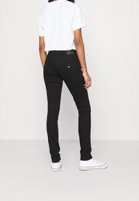 Jeans ajustados negros con bolsillos traseros, una etiqueta de cuero y costuras blancas, combinados con una camiseta blanca lisa y zapatillas blancas.