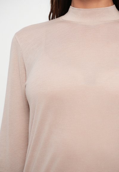 Gaiši rozā turtlenecks, izgatavots no mīksta, ribota auduma. Ar garām piedurknēm un pieguļošu siluetu. Gluda tekstūra, minimālistisks dizains.