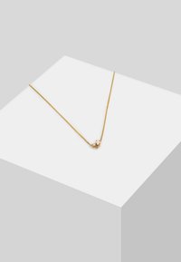 Collana d'oro con una fine catena e un piccolo accento di pietra colorata al centro. Design semplice su uno sfondo grigio chiaro.