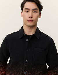 Fekete ingdzseki puha textúrával, egyetlen mellzsebből áll, és egy fokozatos dizájnt mutat, ami lefelé egy rozsdás narancssárga árnyalatba megy át.