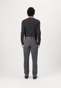 Camisa de manga larga gris oscuro combinada con jeans gris oscuro. Los jeans tienen un corte recto y dos bolsillos traseros. Los zapatos son negros con suela plana.