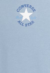 Tela azul claro con el logo "Converse All Star" y una estrella blanca en el centro. Texto en azul oscuro con una textura suave y uniforme.