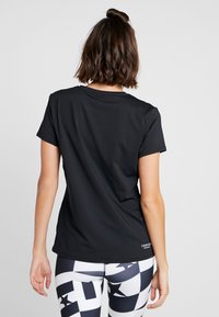 Kobieta o długości włosów do ramion, ubrana w czarną koszulkę z krótkim rękawem i legginsy w czarno-biały geometryczny wzór, stoi tyłem do kamery.