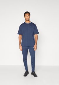 Mørkeblå sport kortærmet t-shirt med rund halsudskæring og logo, parret med matchende tætsiddende bukser og sorte sneakers.