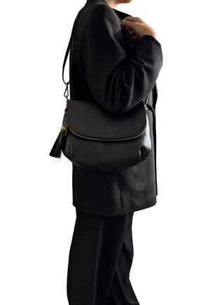 Borsa a tracolla in pelle nera con design curvo, chiusura con zip e un accento a nappina. Indossata a tracolla con una lunga cintura regolabile.