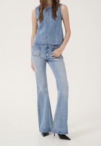 Denim sleeveless top och utsvängda jeans i ljusblått. Toppen har en rak design och rå fåll; jeansen har fickor och en subtil blekning. Svarta klackar.