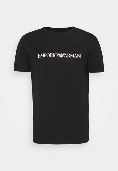 Črna bombažna majica s kratkimi rokavi, ki ima bel natiskan logotip z napisom "EMPORIO ARMANI" čez prsi ter okrogel izrez.