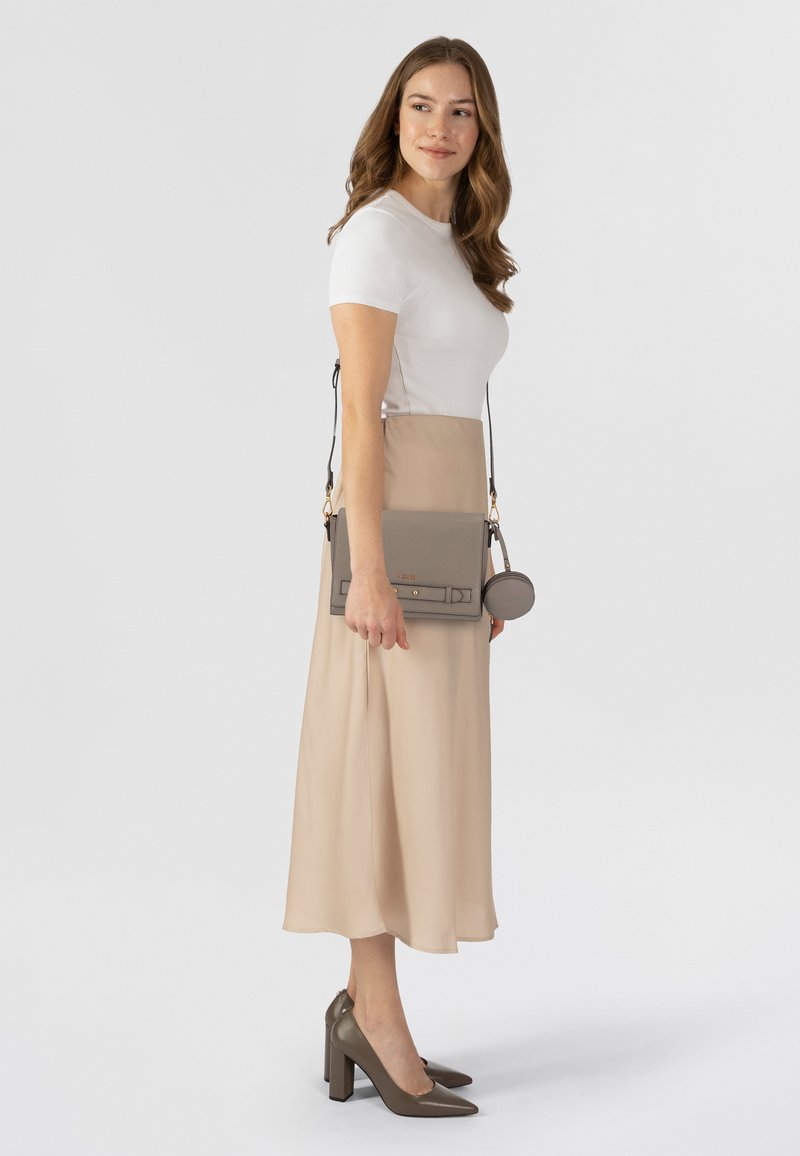 Beiges Midikleid mit enganliegendem Oberteil und schwingendem Rock, kombiniert mit einer grauen Leder-Schultertasche und passenden Blockabsatzschuhen.