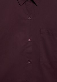 Camisă button-up de culoare violet închis, cu un buzunar pe piept, având un guler ascuțit și patru butoane vizibile pe față.