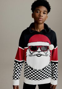 Gebreide trui in zwart, wit en rood; heeft een Santa-ontwerp met zonnebril, een pompon op de kraag en een geruit patroon.