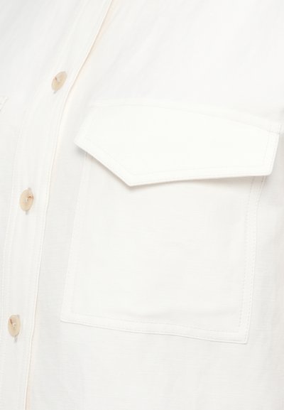 Λευκό πουκάμισο με κουμπιά, με τσέπη στο στήθος, απαλή ύφανση και διακριτικές ραφές. Τα κουμπιά είναι ανοιχτό μπεζ και στρογγυλά.