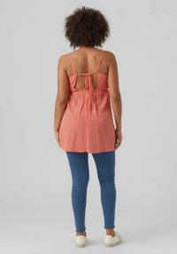 Top senza maniche color pesca con un nodo sulla schiena, tessuto texturizzato e vita arricciata, abbinato a jeans slim blu e sneakers bianche.