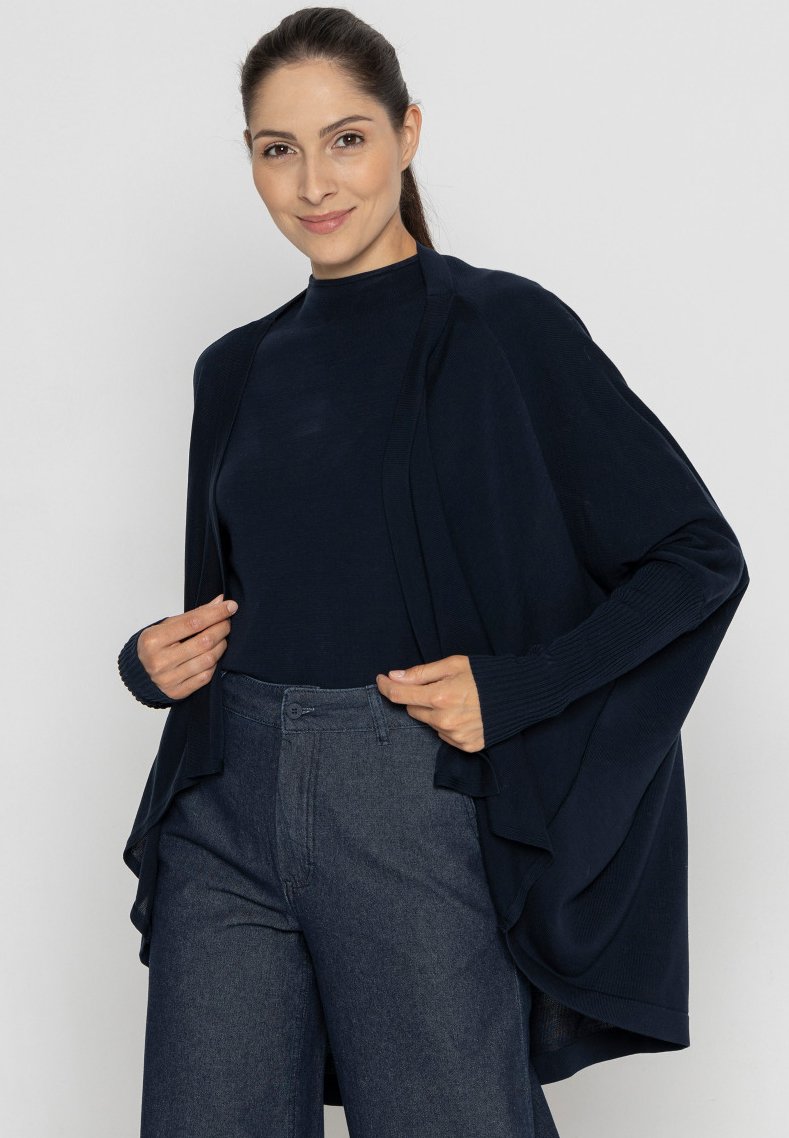 Granatowy sweter z dzianiny z otwartym przodem, długimi rękawami i teksturowanym wykończeniem. W połączeniu z ciemnoniebieskimi spodniami dżinsowymi o wysokim stanie.